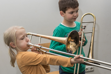 Foto von Kindern, die im Instrumentenkarussell die Posaune ausprobieren.