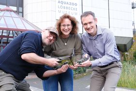 Jörg Mazur, Sandra Honigs und Dr. Jochen Reiter (von links) stehen vor dem Aquazoo und halten drei Bronzeskulpturen sowie ein kleines Terrarium mit einem Feuersalamander in den Händen