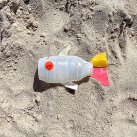 Im Sand ist aus mehreren Plastikteilen ein Fisch zusammengesetzt