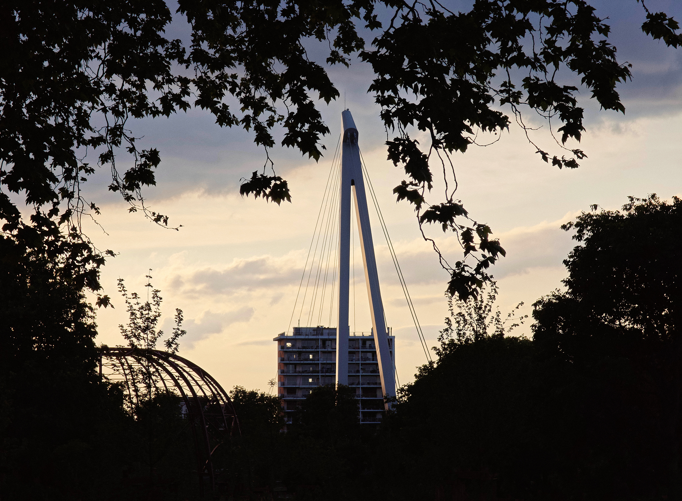 Eine Fußgängerbrücke am Abend von der Île du Ramier über die Garonne in Toulouse mit dem Stadtpanorama im Hintergrund.