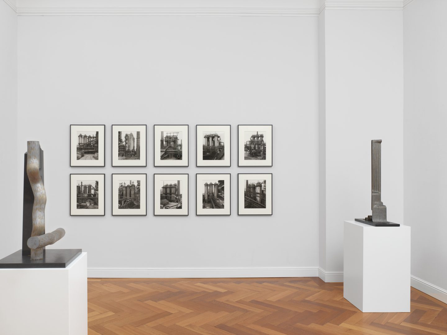 Ausstellungsansicht, Bernd & Hilla Becher, Hochöfen (Winderhitzer), 1982-1988, 10 Silbergelatineabzüge, 10-teilig. Links: Brigitte & Martin Matschinsky-Denninghoff, Denkmal (Stein IV), 1988, Messing und Zinn auf Schiefersockel. Rechts: Lynkeus, 1977, Messing und Zinn auf Holzsockel