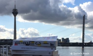 Foto von Rheinuferpromenade mit Fernsehturm im Hintergrund und Büchern im Vordergrund.