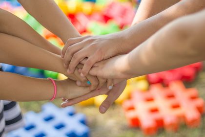 Mehrere Kinderhände aufeinandergelegt signalisieren Zusammenhalt