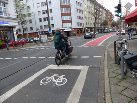 Foto von Lastenradfahrerin auf dem neu markierten Radfahrstreifen mit Roteinfärbung im Kreuzungsbereich