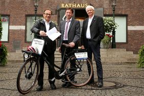 Bürgermeister Reiner Breuer übergibt per Pedes die Neusser Bewerbung für die Tour de France an Düsseldorfs Stadtdirektor Burkhard Hintzsche und Bürgermeister Günter Karen-Jungen. Foto: David Young