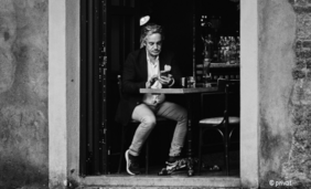 Schwarzweiß Foto von einem Mann an einem Bistrotisch in einem Türeingang