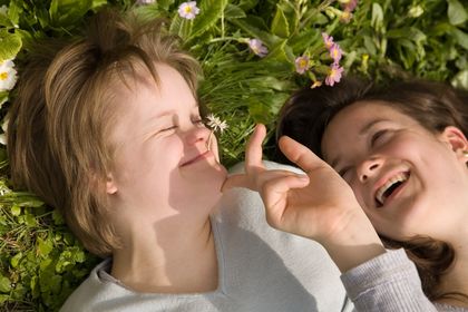 Mädchen mit Downsyndrom liegt mit ihrer Schwester im Gras, ©philidor, fotolia