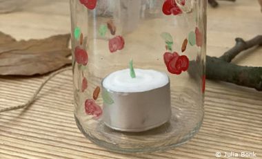 Foto von Teelicht in einem alten Marmeladenglas, das mit Obstmotiven bemalt wurde.