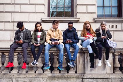 Sechs Jugendliche, die nebeneinander auf einem Steingeländer sitzen und Smartphones in der Hand haben