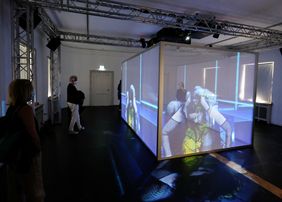 Im Zentrum der Ausstellung steht ein fast transparenter Kubus, der mit hunderten von Aufführungssequenzen die Betrachterinnen und Betrachter in seinen Bann ziehen will; Foto: Wilfried Meyer