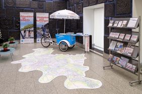 Foto vom Promostand zum Weltfahrradtag. Im Vordergrund der FAhrradplan als Vinylbodendruck und im Hintergrund ein Lastenrad sowie zwei RollUps mit der Aufschrift: "Düsseldorf radaktiv" und "Umdenken & Aufsteigen"