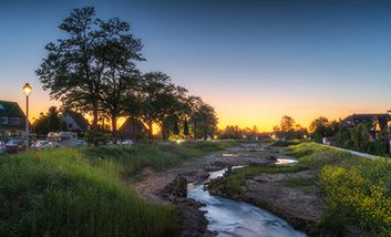Die renaturierte Südliche Düssel bei Sonnenuntergang mit Häusern auf beiden Seiten.