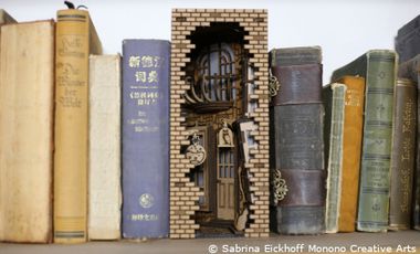 Foto von Buchrücken auf einem Bücherregal. Dazwischen eine Miniaturgasse.