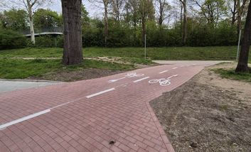 Foto von einem rot gepflasterten Radweg der über eine Wiese führt.