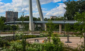 Eine Fußgängerbrücke von der Île du Ramier über die Garonne in Toulouse mit einem begrünten Platz im Vordergrund.