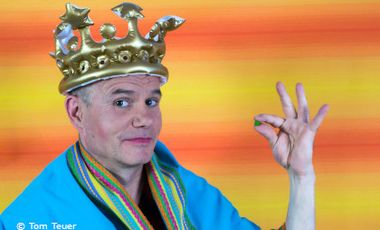 Foto von einem Mann mit einer Krone auf dem Kopf und einer Erbse zwischen den Fingern.