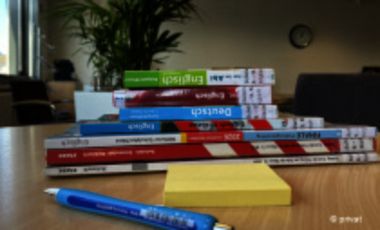 Foto von einem Bücherstapel, Notizzetteln und Stift auf einem Tisch in einer Bibliothek