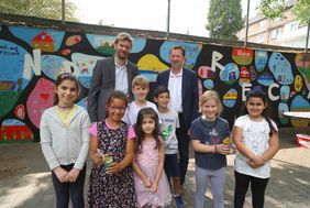 Stadtdirektor Burkhard Hintzsche (hinten r.) und Florian Dirszus, stellv. Leitung Schulverwaltungsamt, mit den Kindern, die im Rahmen des Awo-Projektes zu Kinderrechten an der GGS Sonnenstraße eine Schulhofmauer künstlerisch gestalteten; Foto: Lammert