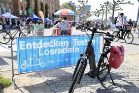 Foto von BAnenr mit dem Motto "Entdecken.Testen. Losfahren. Im Hintergrund die Veranstaltungsfläche mit Fahrrädern und Besuchern.