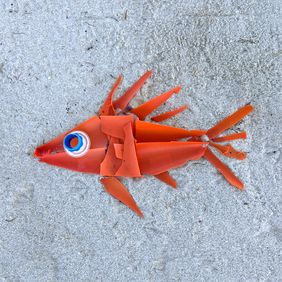 Aus vornehmlich roten Plastikpartikeln ist ein Fisch in den Sand gelegt. 