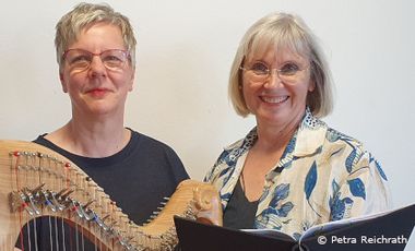Zwei Frauen lächeln in die Kamera, links mit Harfe, rechts mit Gesangbuch