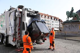 Müllsammelfahrzeug in Aktion mit Papiertonne und zwei Mitarbeitenden des Entsorgers