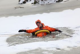 Ausgerüstet mit Schutzkleidung bricht ein Düsseldorfer Feuerwehrmann absichtlich ins Eis ein, um die Eisrettung zu simulieren, ein gesicherter Retter hält ihn über Wasser. Foto: Ingo Lammert