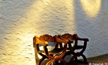 Foto von zwei Holzstühlen an einer weißen Wand mit Lichtreflexen auf der Wand.