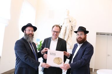 Anlässlich des Pessach-Festes überreichte der Rabbiner Chaim Barkahn (l.) eine handgemachte Mazzah Schemurah, einen Laib ungesäuertes Brot, an Oberbürgermeister Dr. Stephan Keller. Begleitet wurde er von Rabbiner Levi Hefer (r.), Foto: Lammert