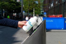 Hand hält Trinkflasche in den Wasserzulauf eines Trinkbrunnens