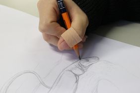 Eine rechte Hand hält einen Bleistift und zeichnet einen Papuawaran auf ein Blatt Papier
