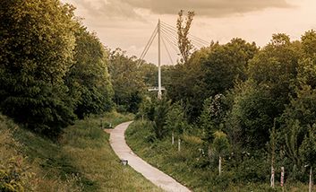 Ein begrünter Weg am Abend, der zu einer Fußgängerbrücke über die Garonne auf die Île du Ramier in Toulouse führt.