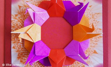 Origami Kraniche aus rotem, orangen und purpur Papier zu einem Kreis gelegt.