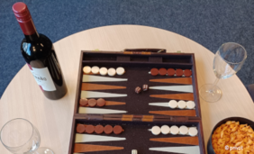 Foto von einem Backgammonspielfeld neben einer Flasche Rotwein, zwei Weingläsern und einem Schälchen mit Knabberzeug