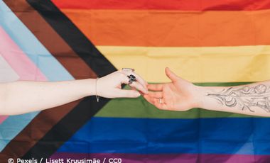 Foto von zwei Händen, die sich vor einer Queer-Flagge berühren