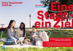 Drei Personen beim Picknick auf Rheinwiese mit Rheinturm im Hintergrund