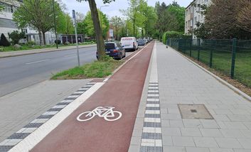 Foto von neuem Radweg. Der Radweg ist in rotem Asphalt ausgebaut und durch einen weißen Trennstreifen optisch vom Gehweg getrennt.