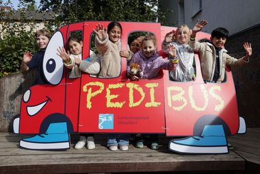 Foto von einer Gruppe Kinder, die hinter einem aus Pappe gebastelten Bus stehen.