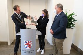 Zur Erinnerung an den Empfang zur Feldhockey-Meisterschaft überreichte Oberbürgermeister Dr. Stephan Keller der DHC-Teamkapitänin Selin Oruz und Dr. Klaus Grossmann, 1. Vorsitzender des DHC, eine gravierte Jan-Wellem-Glasplatte; Foto: Gstettenbauer