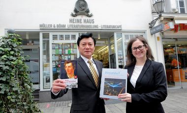 Der chinesische Generalkonsul Feng Haiyang und die Leiterin des Büros für Internationale, Regionale und Europäische Angelegenheiten, Jessica Dedic vor dem Heinrich-Heine-Haus, mit jeweils einem Buch aus der Spende