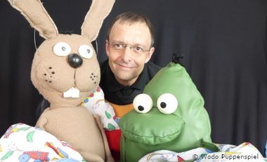 Wodo Puppenspiel: Ein Mann mit zwei Handpuppen, ein Hase und ein Frosch.