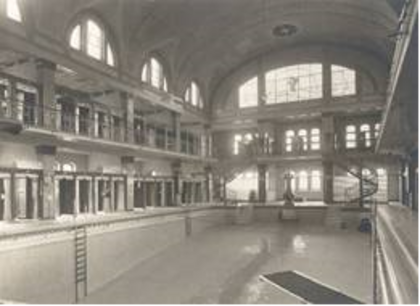 Historische Schwarz-Weiß-Aufnahme der leeren Münster-Therme in Düsseldorf aus dem Jahr 1930 mit Blick auf das große Schwimmbecken und die mehrstöckigen Umkleidegalerien unter einer hohen Gewölbedecke