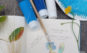 Foto von einem Notizbuch mit Pinsel, Farben und Pflanzen