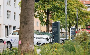 E-Auto parkt an der begrünten Mobilitätsstation Bachplätzchen. Vorne befindet sich eine Ladesäule. 