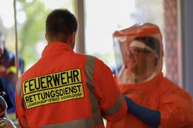 Beim Anziehen der Gebläsefilteranzuege unterstützen die Einsatzkräfte der Feuerwehr Duesseldorf gegenseitig.