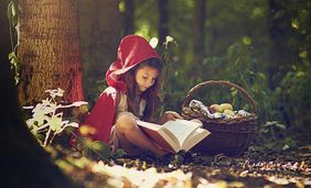 Fotomotiv zu den Märchenwochen 2021 - Rotkäppchen liest im Wald ein Buch