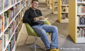 Foto von einem Mann, der in der Bibliothek auf einem Sessel sitzt für die  Ausstellung "Menschen im KAP1"