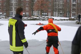 Ausgerüstet mit Schutzkleidung bricht ein Düsseldorfer Feuerwehrmann absichtlich ins Eis ein, um die Eisrettung zu simulieren, vom Ufer aus startet ein gesicherter Retter zur Unglückstelle. Foto: Ingo Lammert