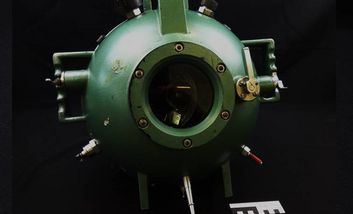 Das Bild zeigt das grüne Gehäuse einer Unterwasser-Filmkamera auf schwarzem Grund.
