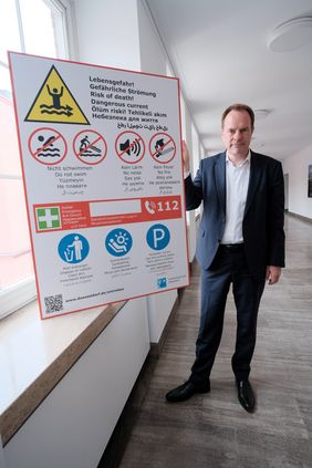 Oberbürgermeister Dr. Stephan Keller mit einem neuen Schild, das eindringlich auf die Lebensgefahr hinweist, die beim Baden im Rhein droht. Foto: Michael Gstettenbauer